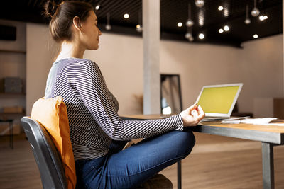 Rear view of woman using laptop at home