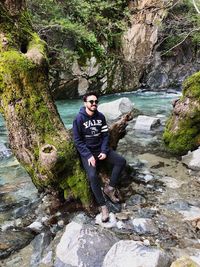 Young man sitting on rock by stream