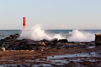 Waves breaking against sea against clear sky