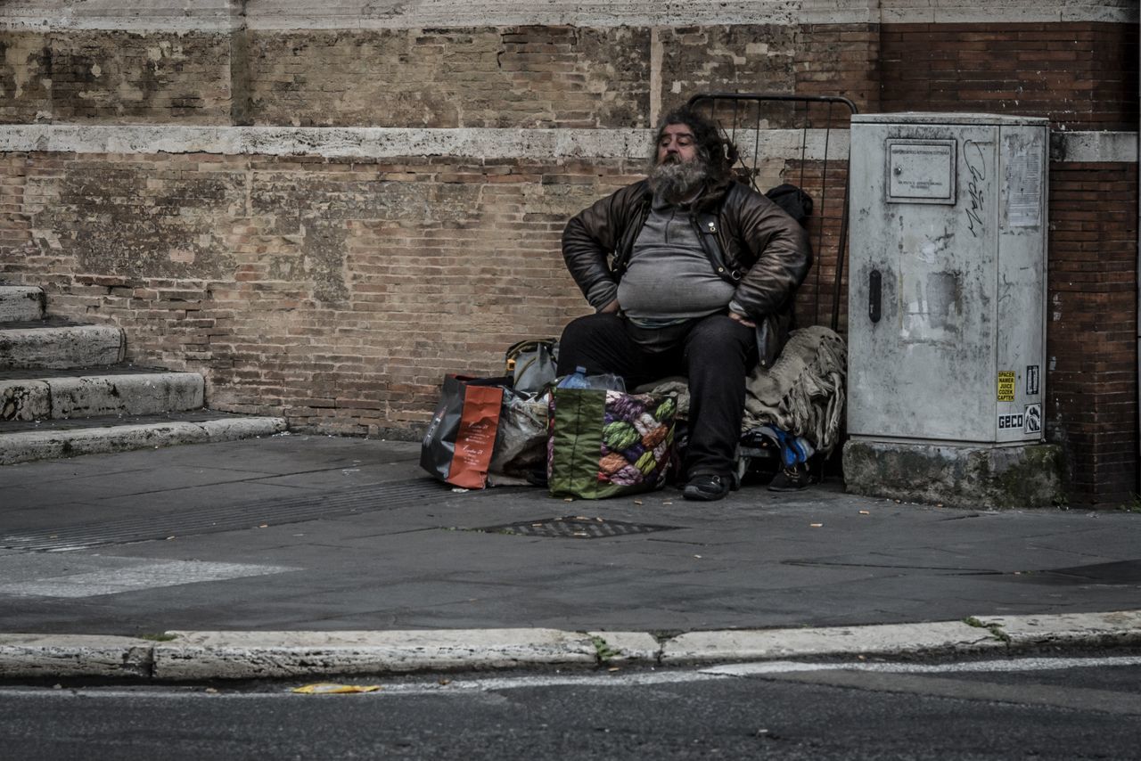 real people, social issues, sitting, full length, architecture, men, one person, city, street, day, clothing, wall - building feature, casual clothing, built structure, wall, lifestyles, outdoors, warm clothing, hopelessness