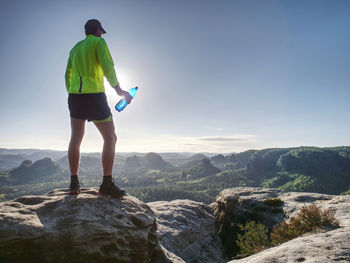 Runner in yellow green shinning jacket and black shorts jumping on rock. man athlete while jumping