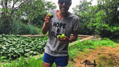 Man holding food while standing by plants against trees