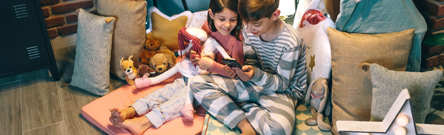 Banner of smiling children looking mobile phone while chatting on social media application at home