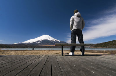 Rear view of man on boardwalk against snowcapped mountain