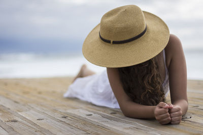 Midsection of woman wearing hat sitting on wood at beach