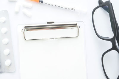 Close-up of medicines with paper and eyeglasses over white background