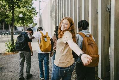 Portrait of happy teenage girl enjoying while walking with friends on sidewalk near fence