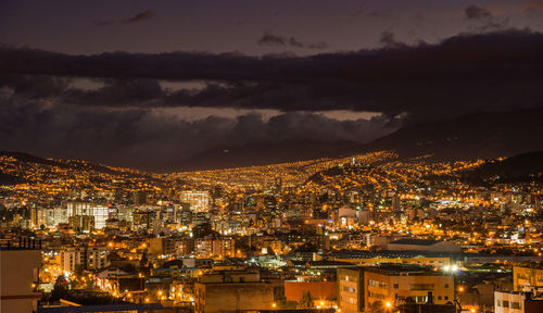 High angle view of illuminated cityscape against cloudy sky at dusk