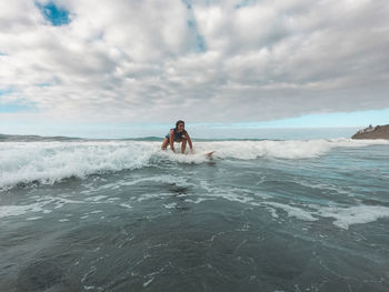 Woman surfing on sea wave against sky