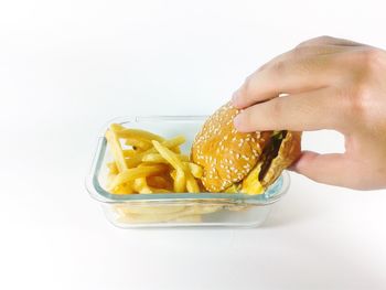 Cropped hand of person holding hamburger in container against white background