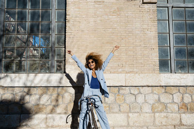 Woman with arms outstretched standing against brick wall