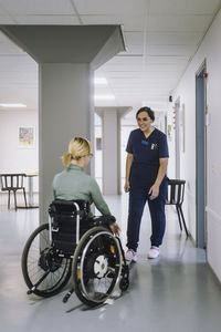 Smiling female healthcare worker walking towards patient with disability at hospital
