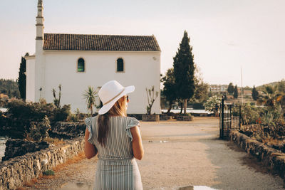 Rear view of woman standing by building against sky