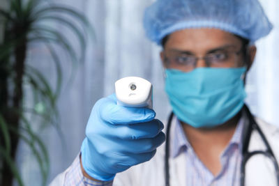 Close-up of doctor wearing mask holding infrared thermometer at hospital