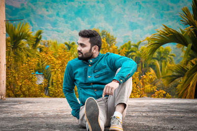 Full length of young man sitting on land against trees