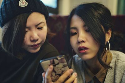 Smiling two women using mobile phone indoors