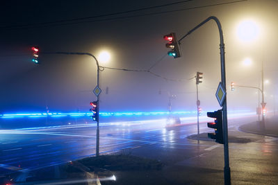 Light trail of emergency ambulance passing crossroad at foggy night.