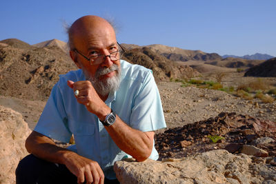 Portrait of senior man standing on rock against clear sky