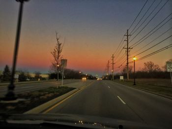 Road passing through forest at sunset