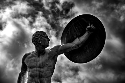 Low angle view statue with shield against cloudy sky