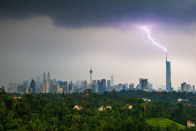 Buildings in city against sky with lightning strikes 