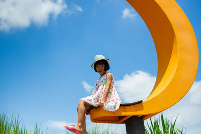 Low angle view of girl sitting against sky