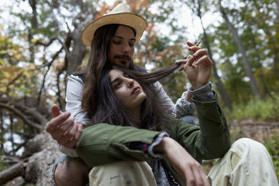 Portrait of young woman holding smart phone while sitting on tree