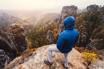 Rear view of man standing on rock looking at mountain against sky