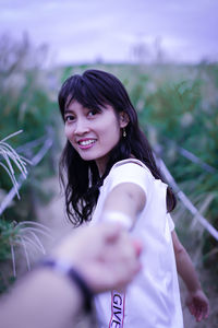 Portrait of smiling young woman holding man hand while standing by plants