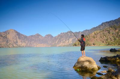 Man fishing standing on rock by lake