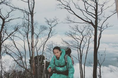 Man standing by bare tree against sky during winter