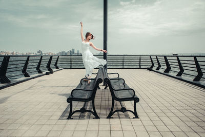 Young woman with arm raised posing on pier over sea