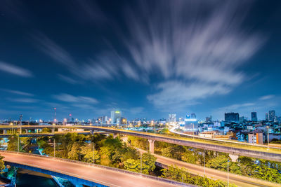 Light trails on bridge in city against sky at night