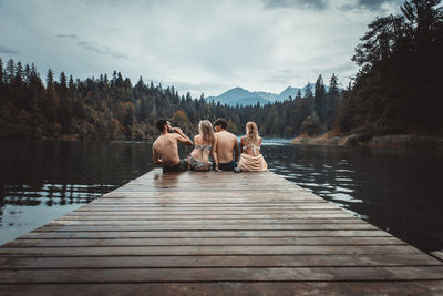 People sitting on pier over lake against sky