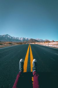 Low section of man on road against clear blue sky