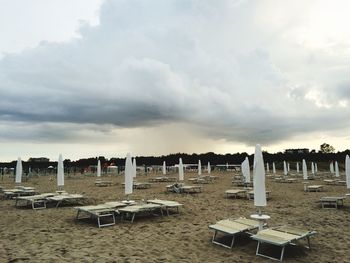 Closed canopies with sun loungers on beach against clouds