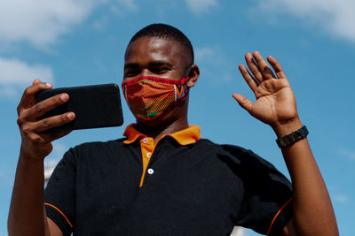 Portrait of man holding smartphone against sky