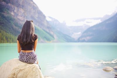 Rear view of woman sitting on rock by lake