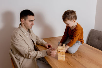 Father and son sitting together at home and playing with wooden blocks. jenga game. 