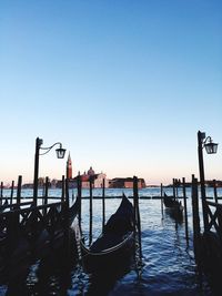 Gondolas moored at harbor with church of san giorgio maggiore in background against clear blue sky