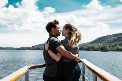 Young couple standing by railing against sky