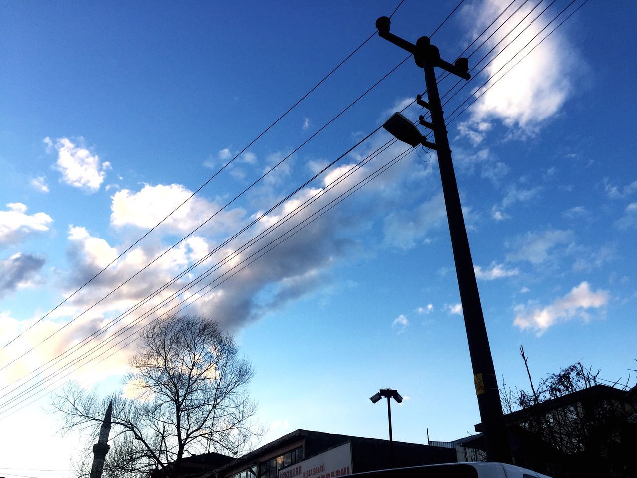 sky, low angle view, electricity, power supply, power line, cable, connection, cloud - sky, technology, no people, outdoors, large group of animals, built structure, bird, day, silhouette, animal themes, building exterior, electricity pylon, animals in the wild, nature, flock of birds, electric pole, architecture, antenna - aerial