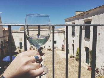 Close-up of hand holding wine glass against clear sky