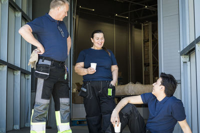 Smiling multi-ethnic workers discussing during coffee break at entrance of distribution warehouse