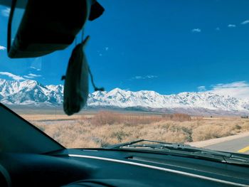 Scenic view of snowcapped mountains against sky seen through car windshield