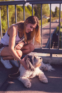 Smiling young woman crouching by dog on footbridge