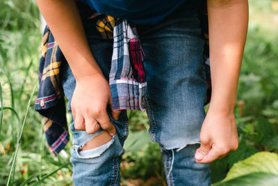 Little boy examines his jeans, torn at the knees.
