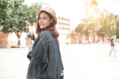 Portrait of smiling young woman using mobile phone in city