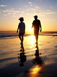 Full length of silhouette friends standing at beach during sunset