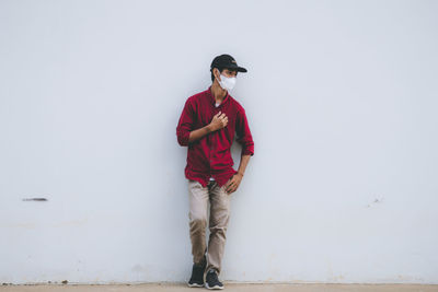 Young man looking away while standing against wall